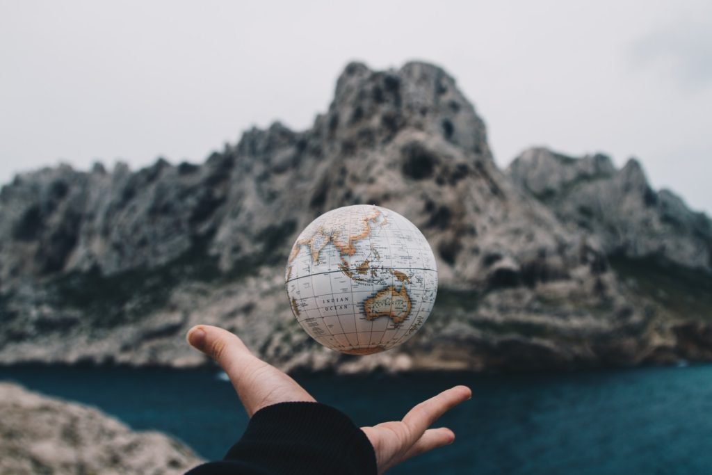 Person tossing globe with rocky land and water in the background