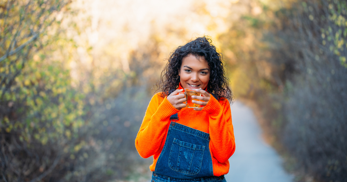 Young lady in fall clothing enjoying herbal tea on a walk outdoors